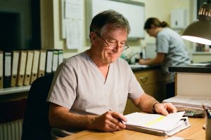 A veterinary practice owner at his desk working through a printed profit-and-loss statement with a calculator.