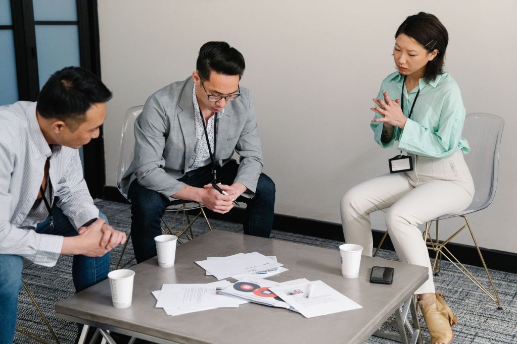 two men and woman in green shirt looking on papers on the table